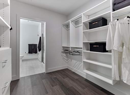 A walk in closet with white shelving and a mirror.