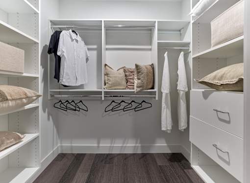 A walk-in closet with white shelves and drawers, containing clothes and pillows.