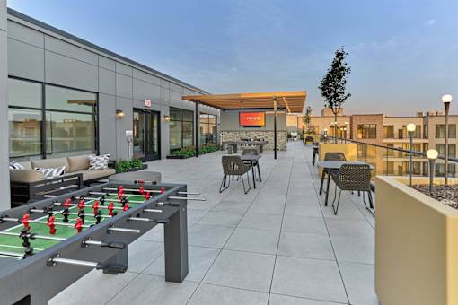 A foosball table is in the middle of a patio with chairs and a barbecue grill.