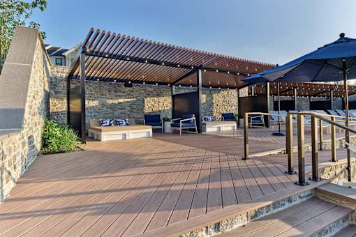 A wooden deck with a stone wall and a pergola.