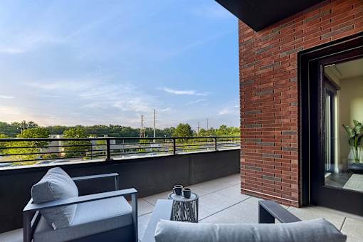 A balcony with a grey couch and a black table.