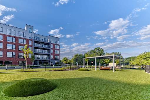 A large grassy area in front of a red brick building with a pavilion.
