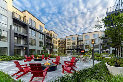 A modern outdoor seating area with red chairs and tables is surrounded by contemporary buildings.