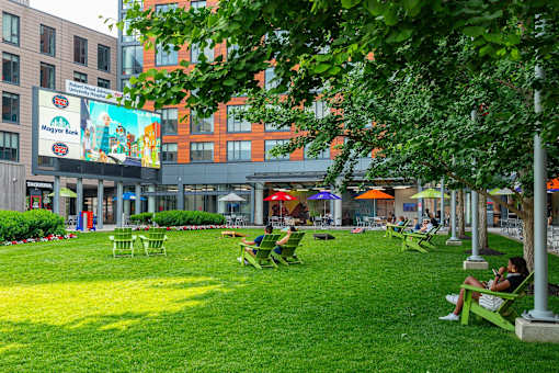 A park with green grass and people sitting on chairs.