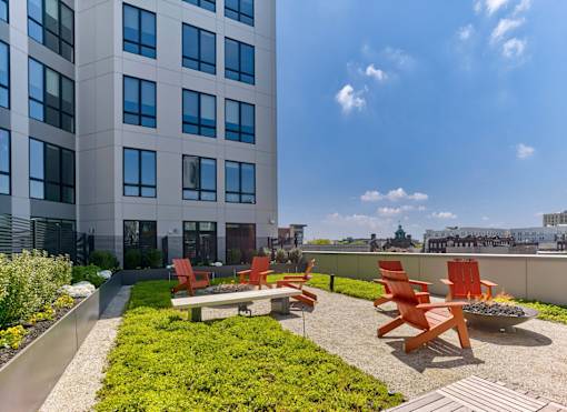 A patio with red chairs and a fire pit in front of a tall building.
