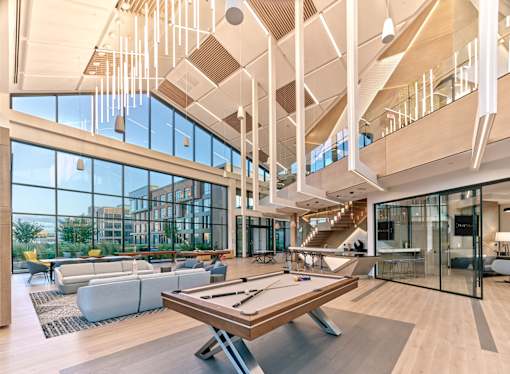 A billiard table is in the middle of a spacious room with a high ceiling and lots of windows.