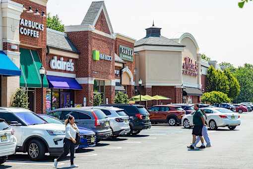 A woman is walking in a parking lot in front of a shopping center.