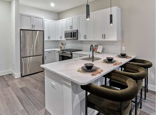 A modern kitchen with a white island and brown chairs.