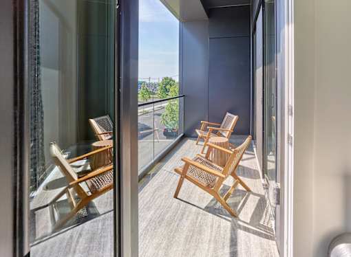 A balcony with two chairs and a table is visible through a glass door.