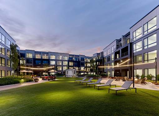A modern building complex with a grassy area in front and several lounge chairs.