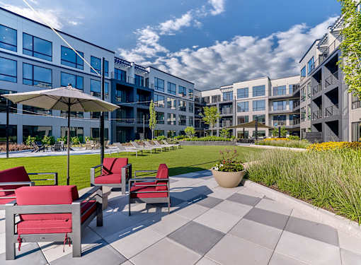 A sunny day at a modern apartment complex with red chairs and umbrellas on the patio.