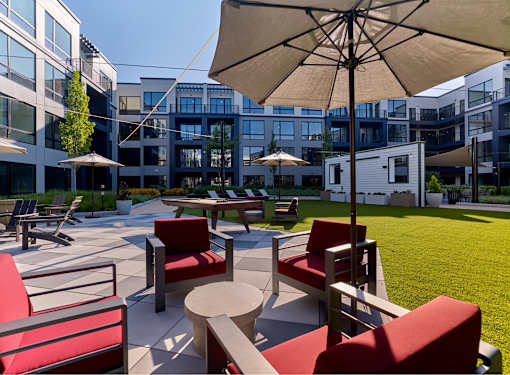 A patio with red chairs and a beige umbrella.
