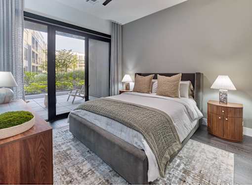 A bedroom with a large bed, a wooden nightstand, and a window with a view of the city.