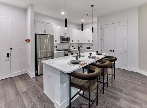 A modern kitchen with a white island and brown chairs.