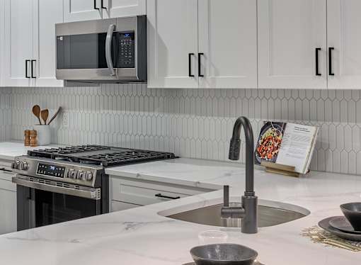 A modern kitchen with a stove, microwave, and white cabinets.