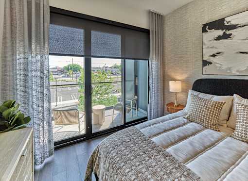 A bedroom with a large bed and a view of the outside through the sliding glass doors.