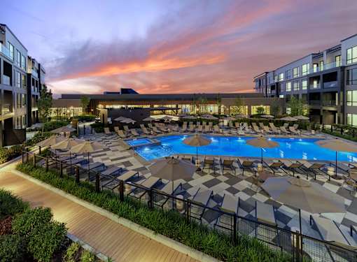 A large outdoor swimming pool surrounded by sun loungers and umbrellas.