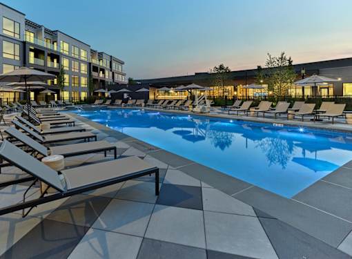 A swimming pool surrounded by sun loungers and umbrellas in front of a building.