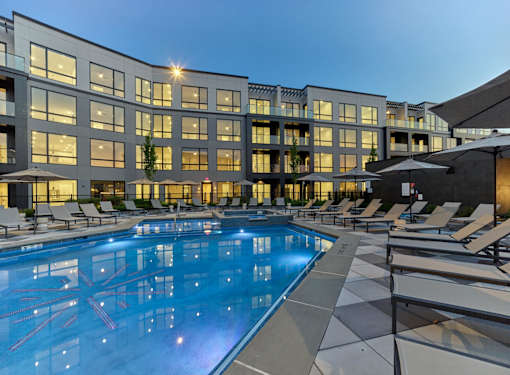 A large swimming pool in front of a modern building with lounge chairs around it.