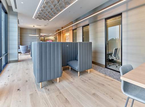 A modern office space with a wooden floor and a grey meeting booth.