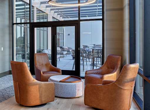 Three tan chairs are arranged around a small table in a room with a glass wall.