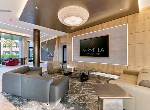 A living room with a grey sofa and a TV screen that says VERMELLA.