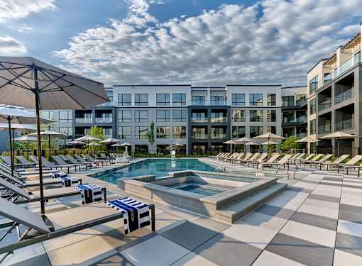 A large outdoor swimming pool with sun loungers and umbrellas in front of a modern building.