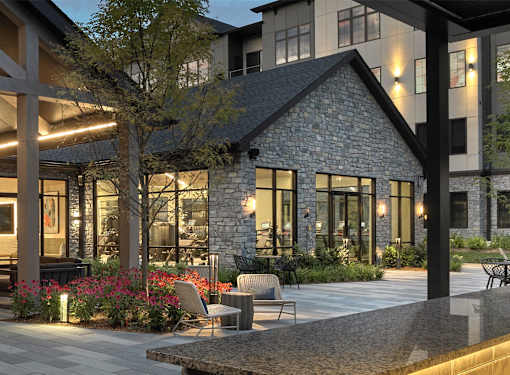 A stone building with a black roof is surrounded by a patio with chairs and a table.