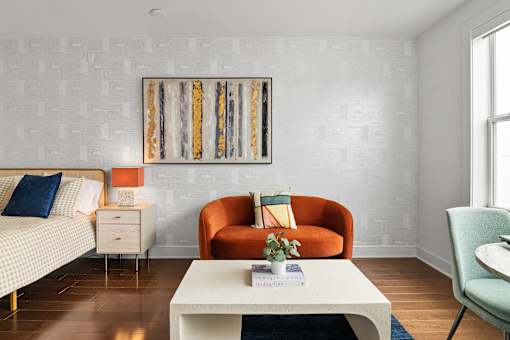 A living room with a white sofa, a white coffee table, an orange chair, and a painting on the wall.