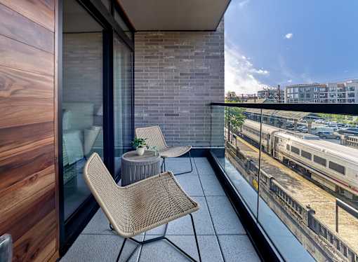 A balcony with a chair and a table overlooking a train track.