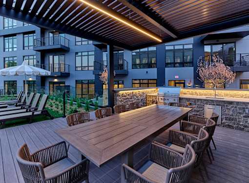 A dining table surrounded by chairs on a deck in a luxury apartment community with resort-style pool.