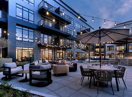 A patio area with tables and chairs is lit up with string lights.