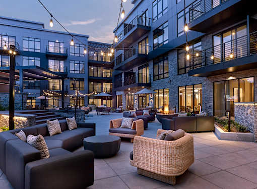 A patio area with couches and tables is illuminated by string lights.