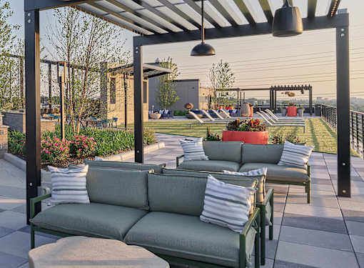 A patio with a green couch and a table with a red planter.