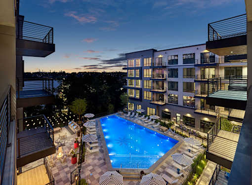 A swimming pool surrounded by lounge chairs and umbrellas is seen from a balcony.