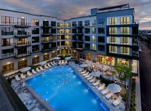 A large swimming pool surrounded by lounge chairs and umbrellas is the focal point of the image.