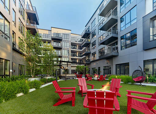 A patio with red chairs and a fire pit in front of apartment buildings.