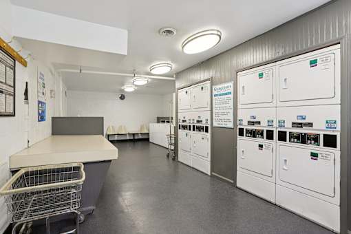 A clean, well-organized laundry room with a shopping cart and washing machines.