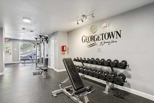 A gym with a row of dumbbells and a bench in front of a wall with the word "Georgetown" on it.