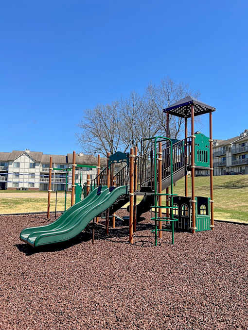 Playground with green slides and climbing structure at River Oaks at Rochester Hills Apartments.