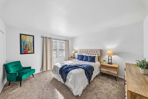 A bedroom with a large bed, a green chair, and a painting on the wall.