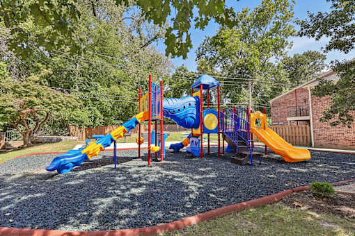 A playground with a blue and yellow slide, a red and yellow slide, and a yellow slide Georgetown of St. Louis Apartments