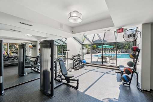 Fitness center at River Oaks at Rochester Hills with weight machines and pool visible through glass wall.
