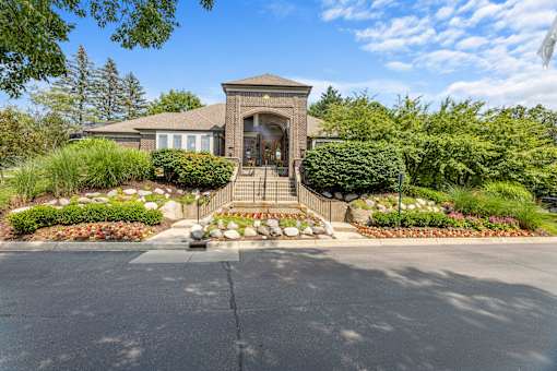 River Oaks at Rochester Hills Apartments clubhouse entrance with stone steps, railings, and landscaped flower beds.