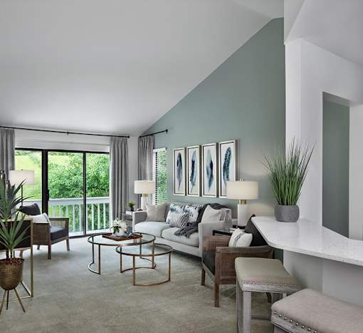 Spacious living room at River Oaks at Rochester Hills Apartments with sofa, accent wall, and sliding glass door to balcony.