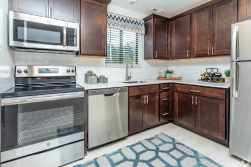Kitchen with stainless appliances, dark wood cabinets, white backsplash, patterned rug at River Oaks in Rochester Hills.