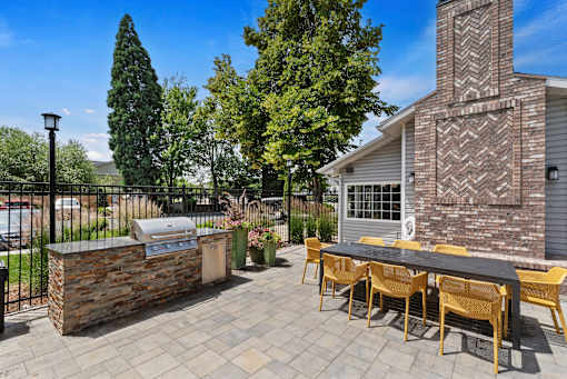 a patio with a grill and a table with yellow chairs