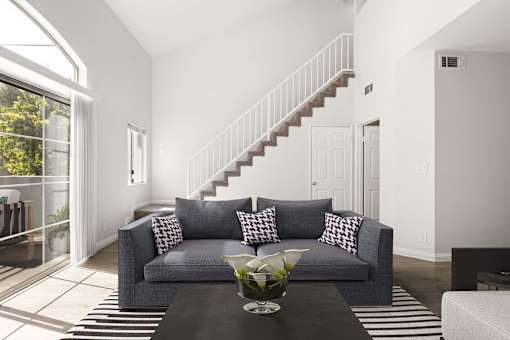 A grey couch with pillows is in the middle of a room with a staircase.