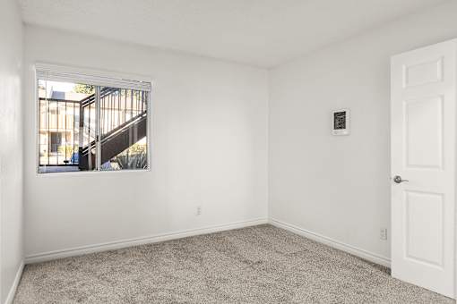 A room with a white door, a window, and a carpeted floor.