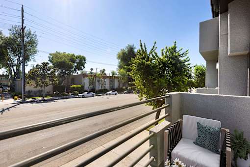 A white chair with a green pillow is on a balcony overlooking a street.